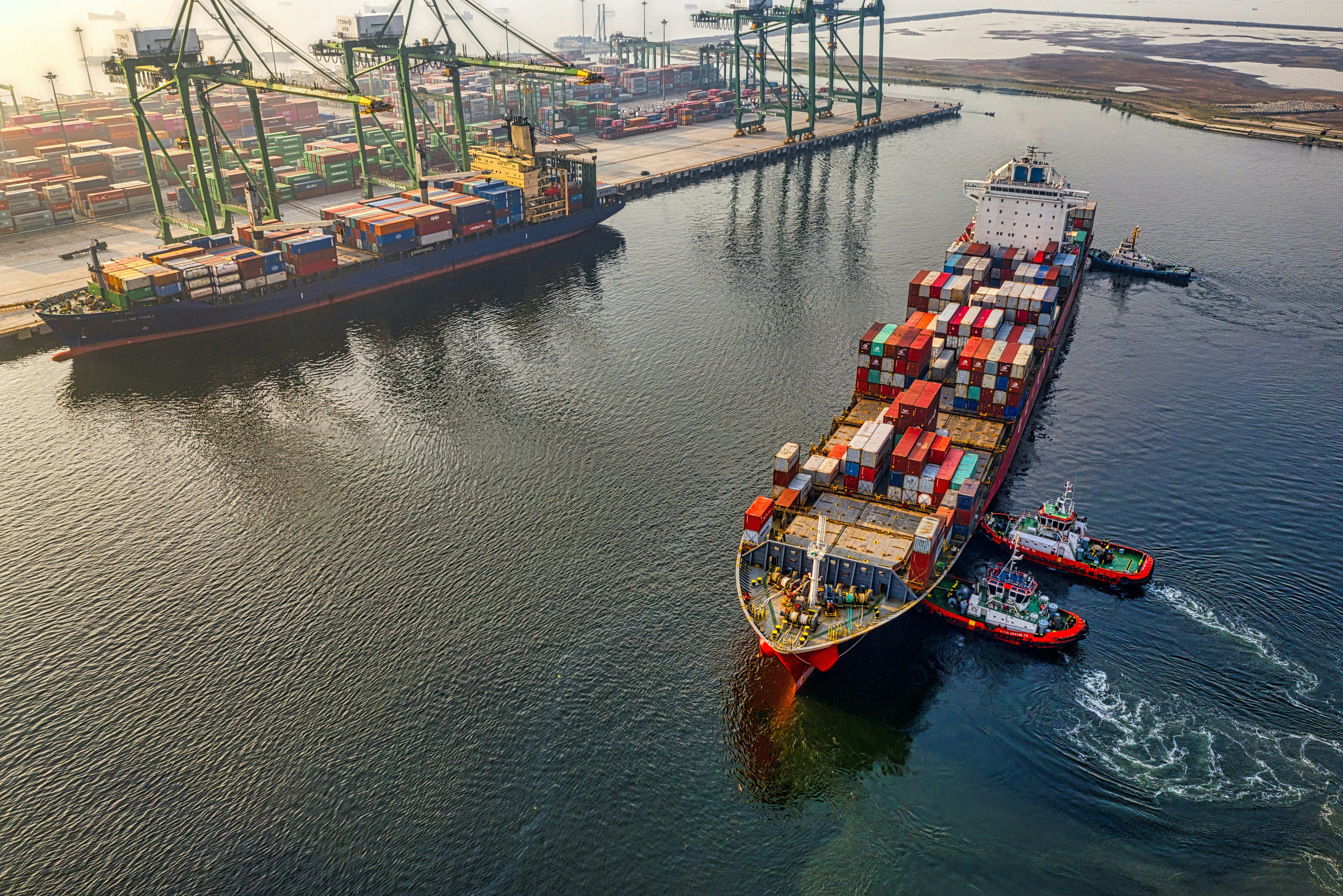 Vista aérea de navios porta-contêineres junto a um terminal marítimo.